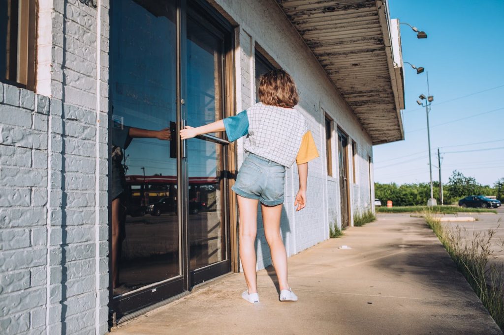 A woman in casual wear opens a glass door on a sunny day at a vintage building in Denton, TX.